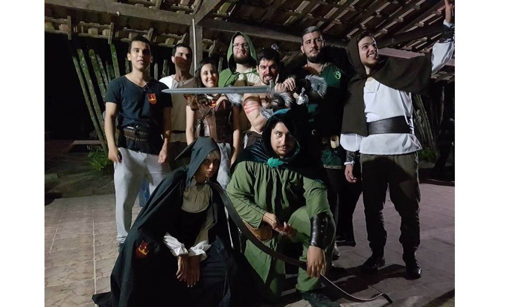 nove personagens de LARP reunidos para o encerramento do evento na noite após um dia jogando. Todos estão vestidos com indumentárias para LARP.